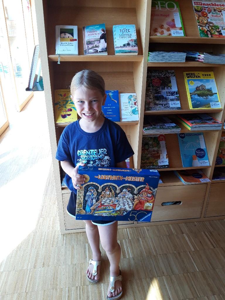 Mädchen mit Spiel in der Bücherei vor einem Regal