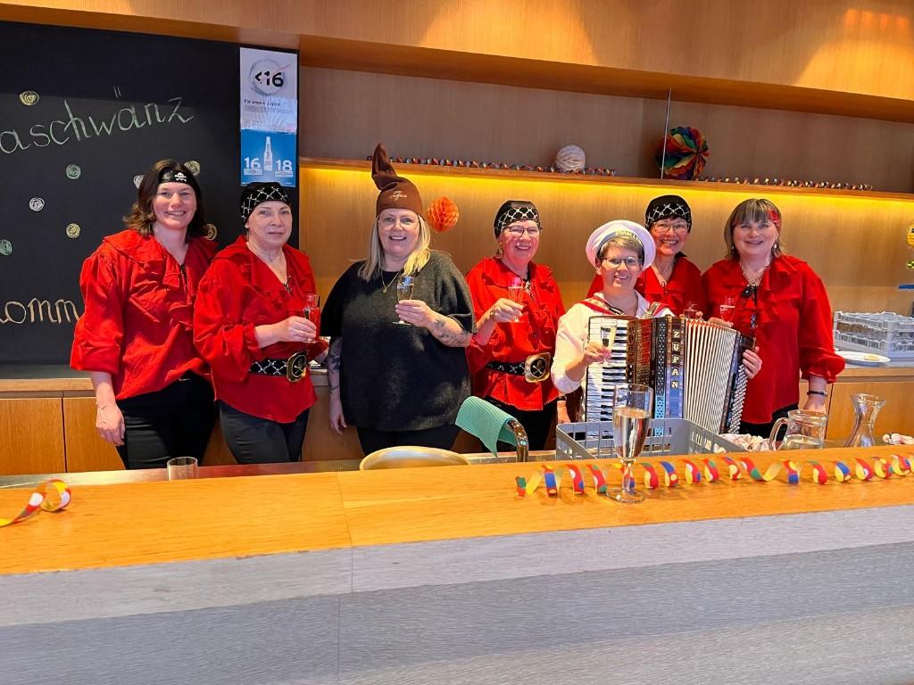 Leute hinter der Budel: Frauen mit rotem Oberteil und eine Frau mit Ziehharmonika