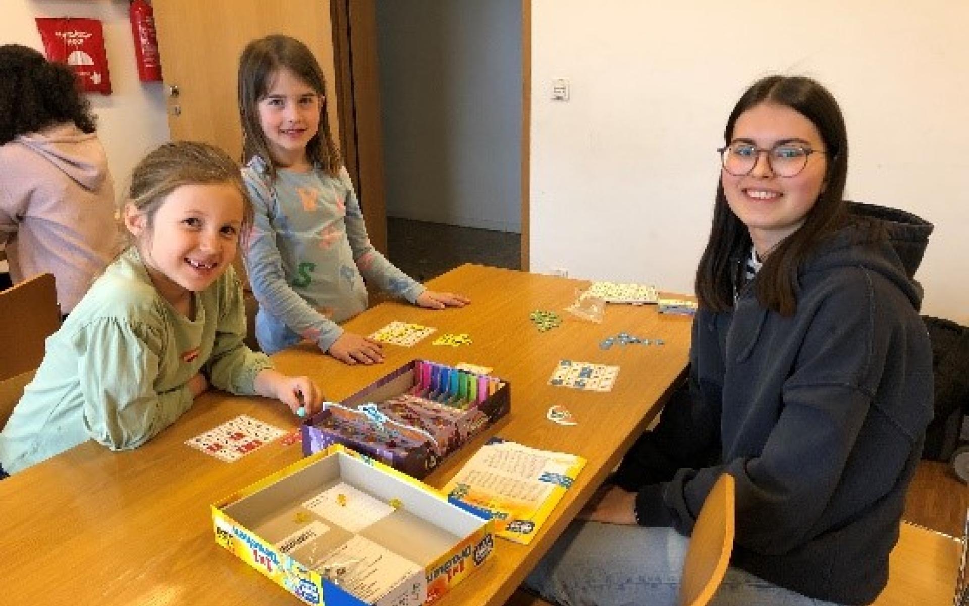 2 Mädchen und eine junge Frau beim Spielen am Tisch sitzend
