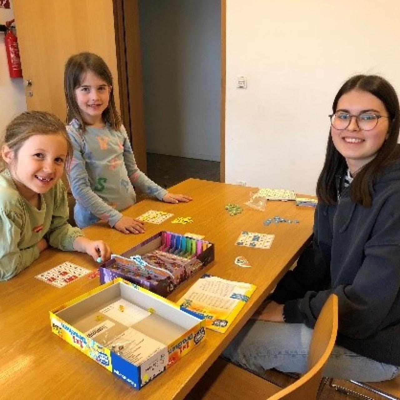 2 Mädchen und eine junge Frau beim Spielen am Tisch sitzend